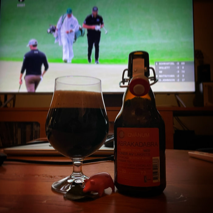 Ölglas och flaska märkt 'Ovanum Abrakadabra' med golf på TV i bakgrunden.