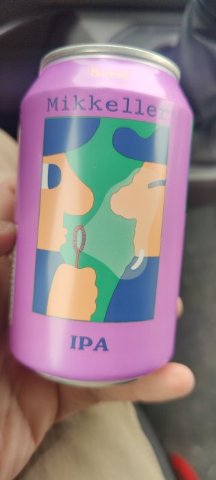 Hand håller en Mikkeller IPA-öldos med färgglatt abstrakt ansiktskonstverk på en lila bakgrund.