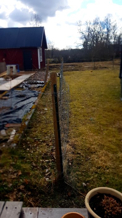 Underhållsfritt stängsel med hål och taggtråd längs en tomtgräns, staketet verkar vara lite böjt.