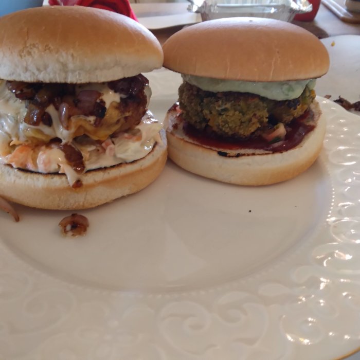 Två hamburgare på tallrik, en med kött och toppings, den andra vegetarisk med gröna biffar och sås.