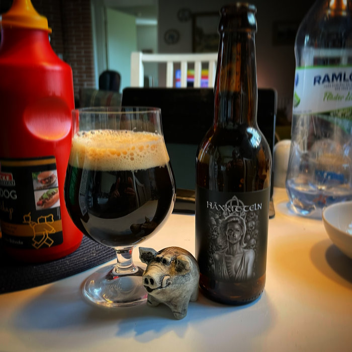 Ett glas mörkt öl, en ölflaska och en liten gristräfigur på ett bord, betyg 3,8/5.
