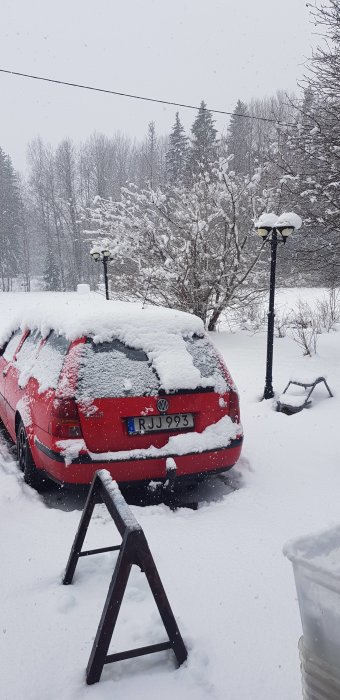 En röd bil täckt med snö under ett kraftigt snöfall.