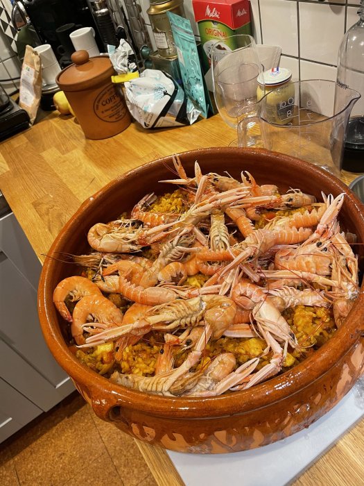 En lergryta full med paella och räkor på ett köksbord.