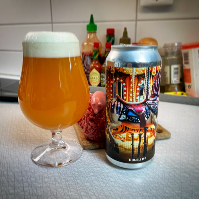 En IPA-öl i glas bredvid färgglad burk och snacks på köksbänk.