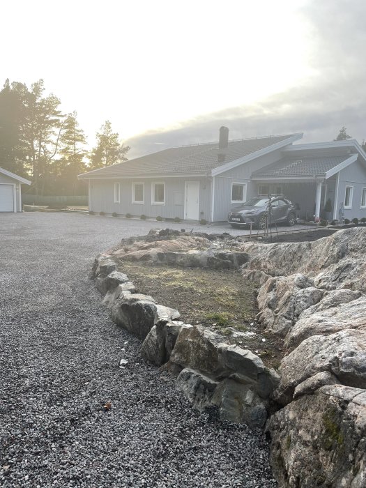 Tom rabatt vid entré med stenkanter och grusväg i ett bostadsområde, redo för beplantering.