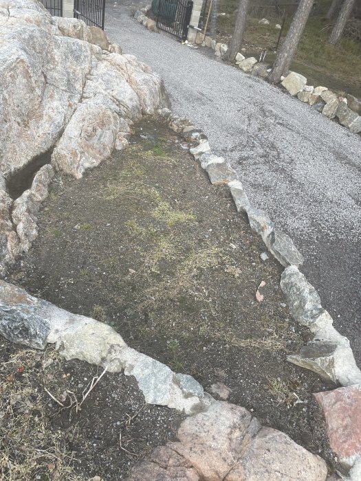 Oplanterad rabatt vid entrén omgiven av stenar och grusväg, redo för landskapsdesign.