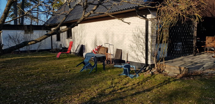 Baksida av ett hus med en liten terrass, lösa stolar och en gavelterrass kopplad till en pergola.