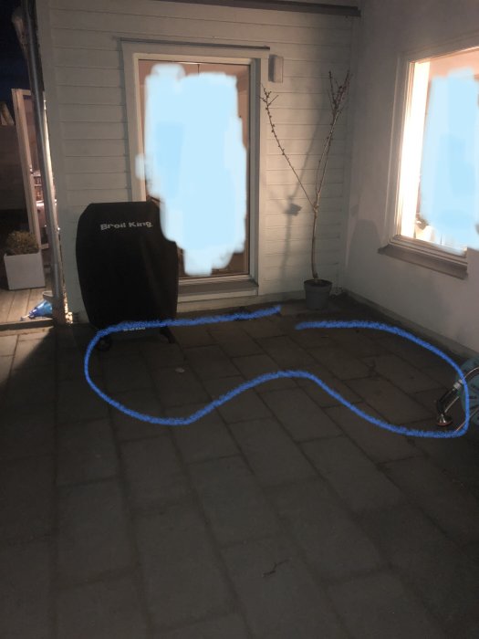 Enhetlig plattsättning med markerat område för planerad rabatt framför husets fönster och dörr.