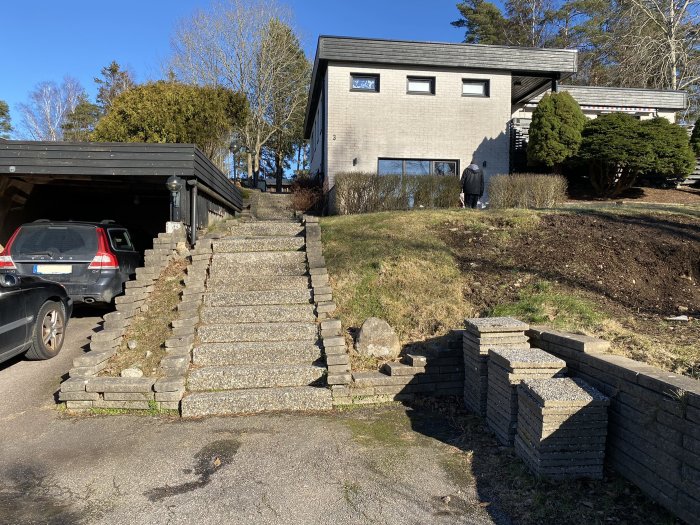 En oorganiserad trädgård med en gammal stentrappa och bil parkerad vid en carport.