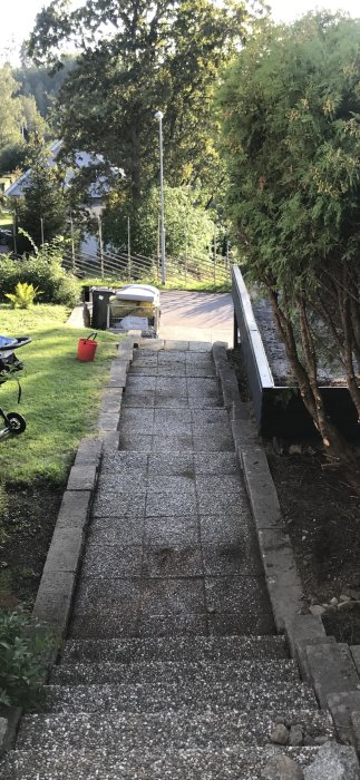 Uppfart i kullersten som leder till en trädgårdstrappa, med carport till vänster och jordhög till höger.