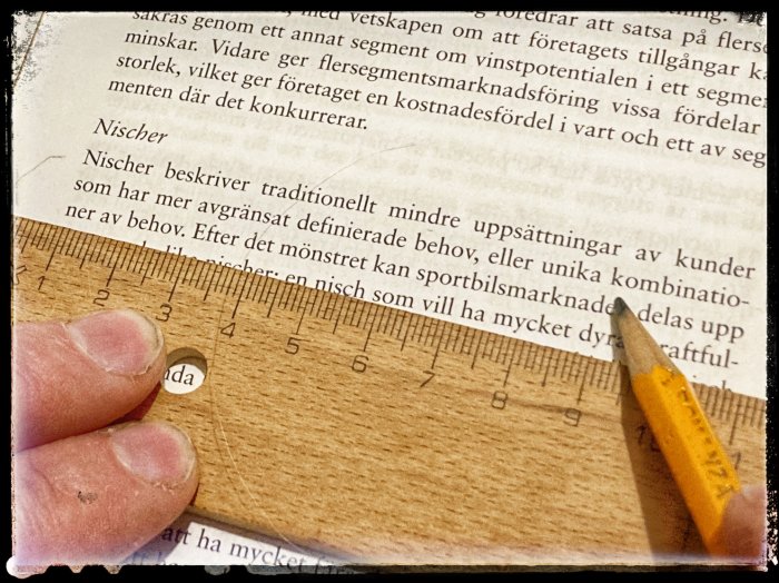 Hand med blyertspenna som pekar på text om nischer och traditionell marknadsföring på papper med linjal.