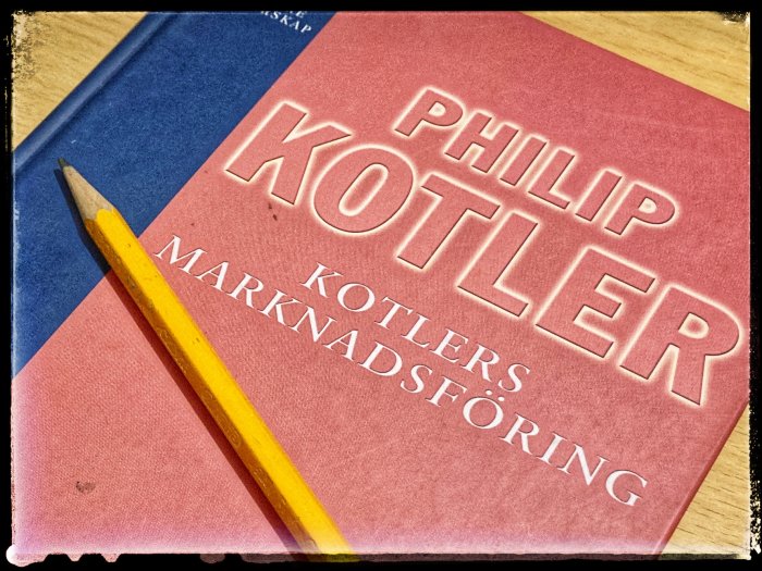 Boken "Kotlers Marknadsföring" av Philip Kotler och en gul blyertspenna på bordet.