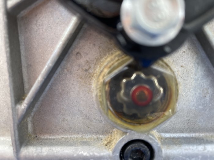 Närbild av en suddig nivåmätare på en kompressor med röd markör och synlig oljenivå.