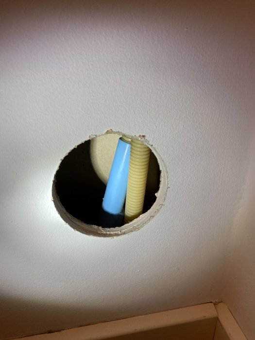 Cirkulärt hål i en vit vägg med felaktigt identifierade flexrör för el, misstaget av en besiktningsman som letade vattenskada.