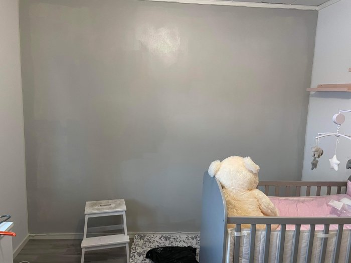 Nyanserad grå målad vägg i barnrum med spjälsäng och stor nallebjörn.