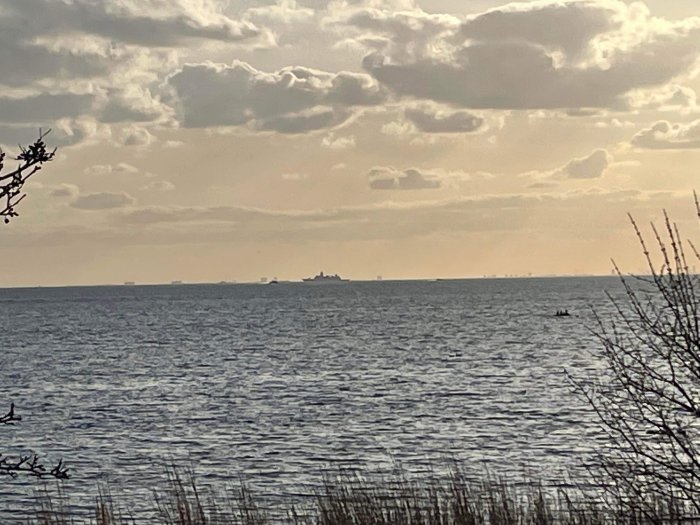 Skepp syns på horisonten över havet under en molntäck himmel vid skymning.