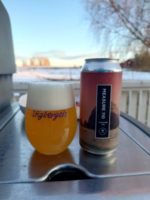 Ölglas och ölburk på ett utebord med suddig bakgrund av vinterlandskap.