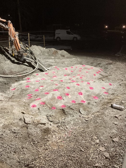 Markborrning utförd i mörker, rosa markeringar på klippformation, grävmaskinsarm och vit skåpbil i bakgrunden.