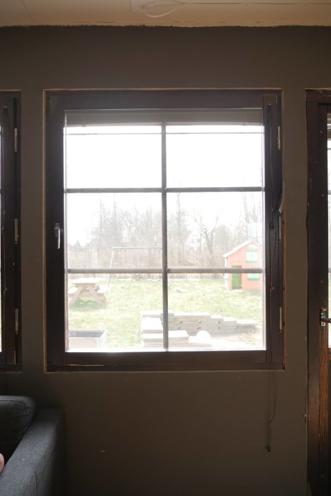 Ett gammalt fönster inne i ett hus, med synlig sidokarm och en utsikt över en bakgård.