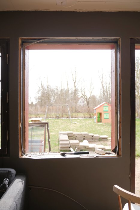 Utsikt genom ett nyligen borttaget fönster, med verktyg synliga, och trädgård i bakgrunden.