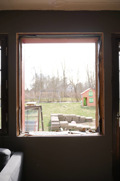Avlägsnat fönster i vardagsrum med utsikt mot trädgård, verktyg ligger på fönsterbrädan.