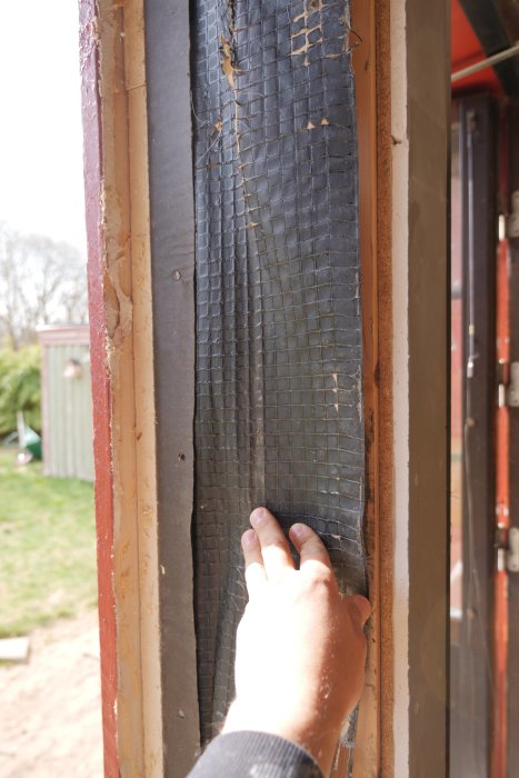 En hand pekar på en uppbruten fönsterkonstruktion med synlig isolering och en del av fönsterkarmen.