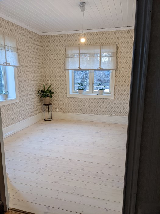 Renoverat matrum med vitmålat trägolv, tapetserade väggar och hängande taklampa.