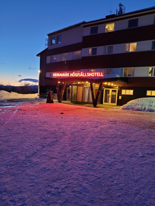 Utsidan av Hemavans Högfjällshotell vid skymning med snö och upplyst skylt.