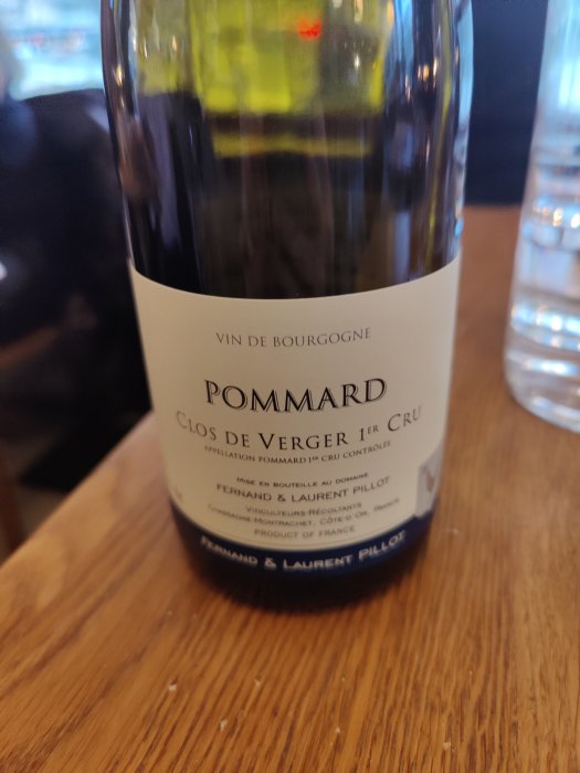 Flaska Pommard Clos de Verger 1er Cru på ett bord, suddig bakgrund.