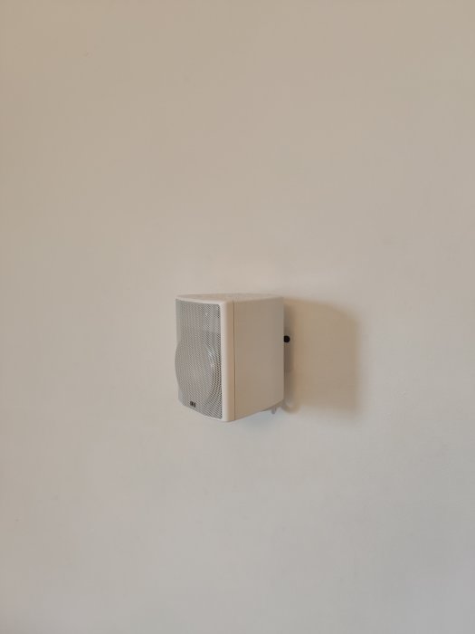Vit centerhögtalare monterad på en ljus vägg i ett hembio-system.