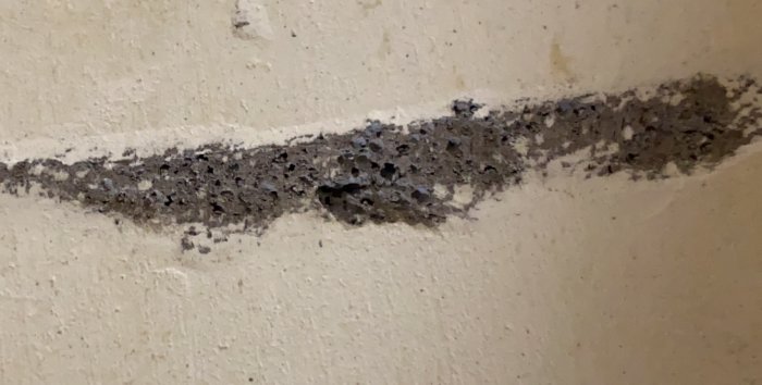 Skadad mellanvägg med poröst material som verkar vara blåbetong, exponerat genom skrapning.