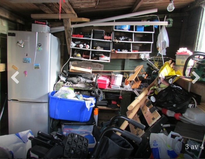 Rörigt garage med diverse föremål, hyllor och en kyl.
