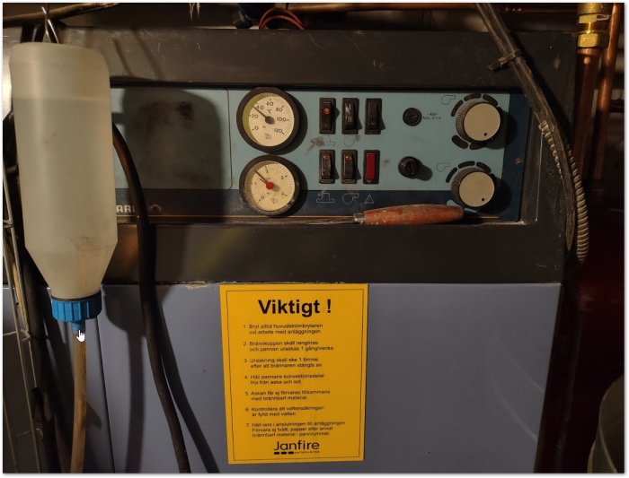 Varmekilde i kjeller, kombinert el/ved-panne med manometer og påfyllingsrør, merket med #1 og #2.