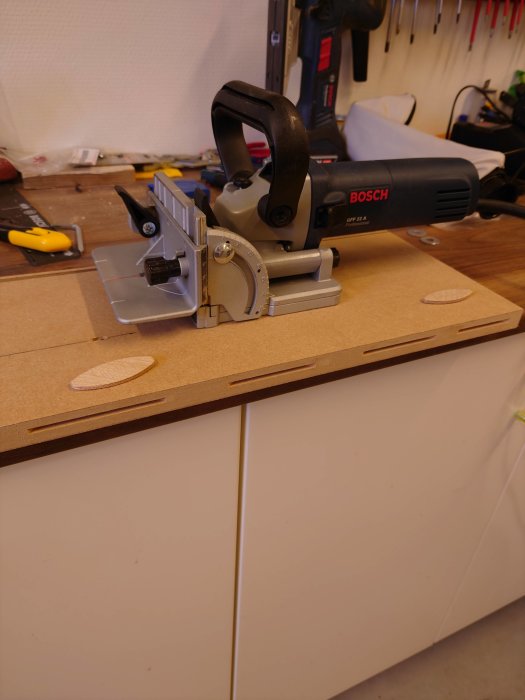 Kexfräs med insatta kex i MDF-skiva på arbetsbänk med verktyg i bakgrunden.