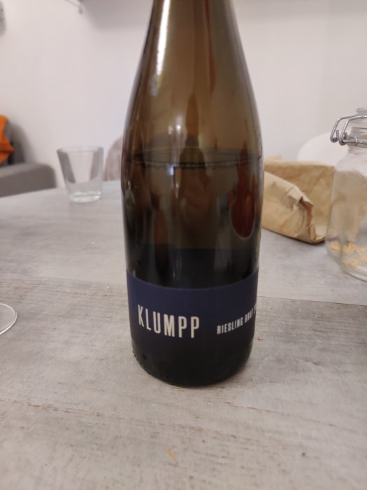 Flaska Klumpp Riesling Sekt på ett bord med oklara bakgrundsobjekt.