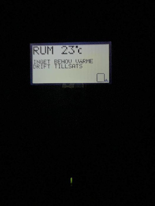 Digital display som visar "RUM 23°C INGET BEHOV VÄRME DRIFT TILLSATS" i mörkt rum.