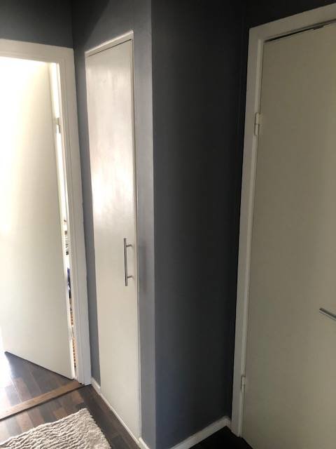 Gammaldags vit garderob med dörrar, i en hall med mörkgråa väggar, behöver renovering.