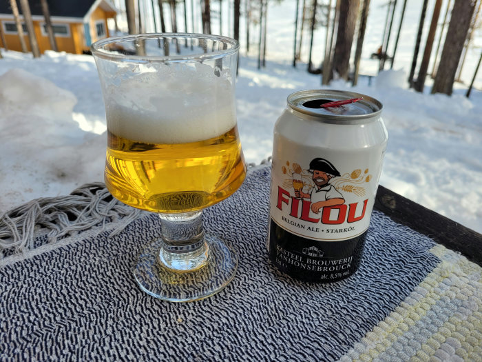 Halvtomt glas med öl och en ölburk Filou på ett bord utomhus med snö i bakgrunden.