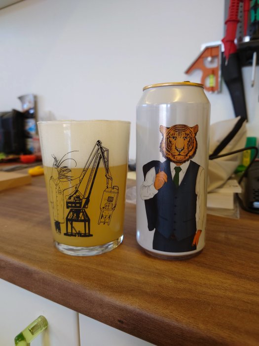 Ölglas med hamnmotiv bredvid ölburk med illustrerad man i kostym och tigerhuvud.