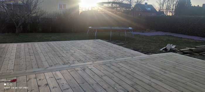 Halvfärdigt trädäck i en trädgård vid solnedgång med byggmaterial i förgrunden.