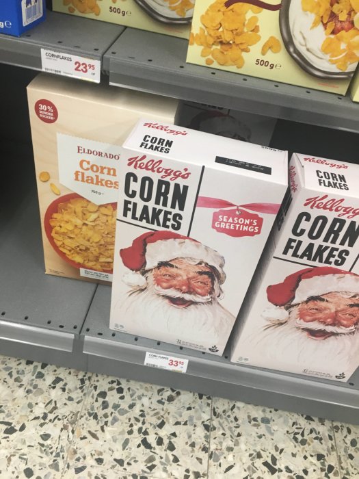 Cornflakes-förpackningar i butikshylla, en med jultema och Kellogg's logga, andra varumärken bredvid.