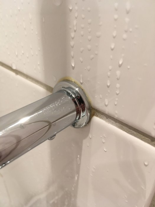 Kromad duscharm fäst vid kakelvägg med lossnande skruvfäste, vattendroppar synliga.