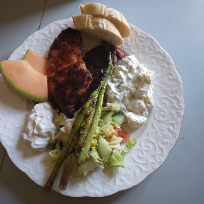 Grillad kycklingfilé och fläsknoisette med sparris, tzatziki, potatissallad på vit tallrik.