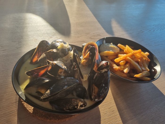 Skål med "Moules marinières" och en sidorätt med pommes frites i solljus.