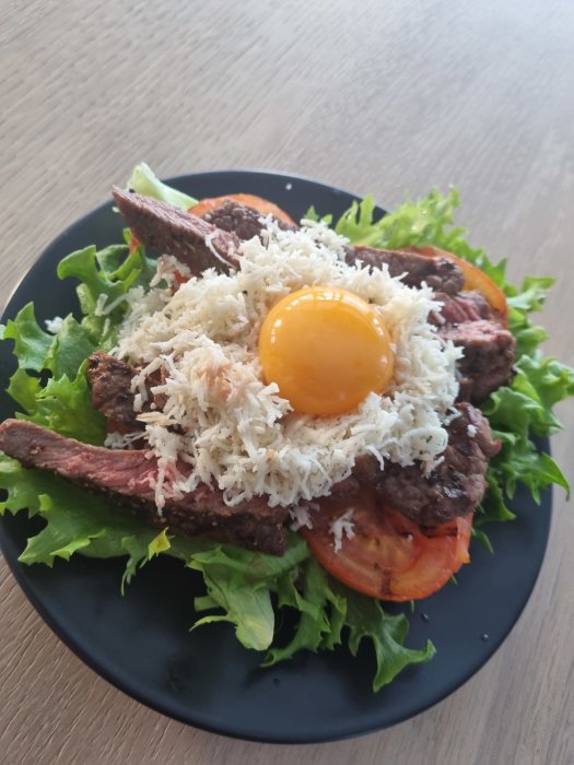 Bookmaker Toast med stekt kött, riven ost, rått äggule på topp, salladsblad och tomat på svart tallrik.