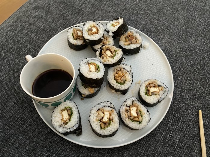 Hemgjord sushi med svamp och tofu på ett fat bredvid sojasås och ätpinnar.