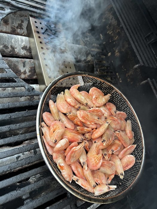 Räkor grillas på en gasolgrill med rök som stiger upp från röklådan.