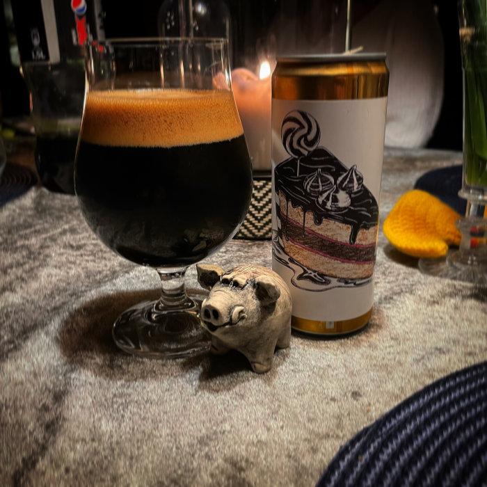 Ett glas mörkt öl bredvid en burk med bakverksillustration och en liten gipsfigur av en gris.