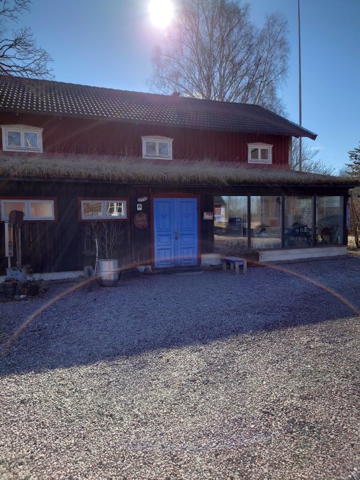 Ett rött trähus med grön dörr, grusgång och grönt tak i soligt väder.