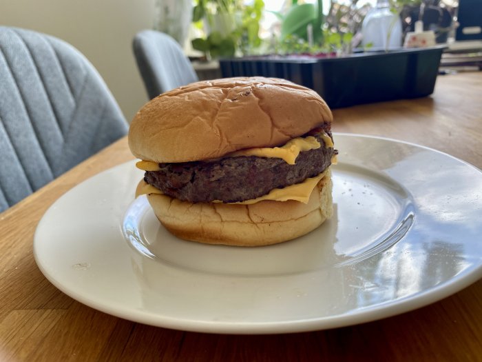 Hamburgare med ost på en Martin's potato roll på en vit tallrik.